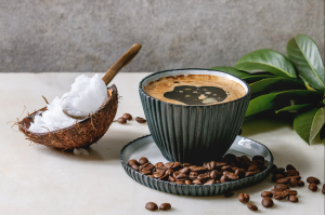 A spoon filled with coconut shavings in a coconut, next to a cup of coffee.